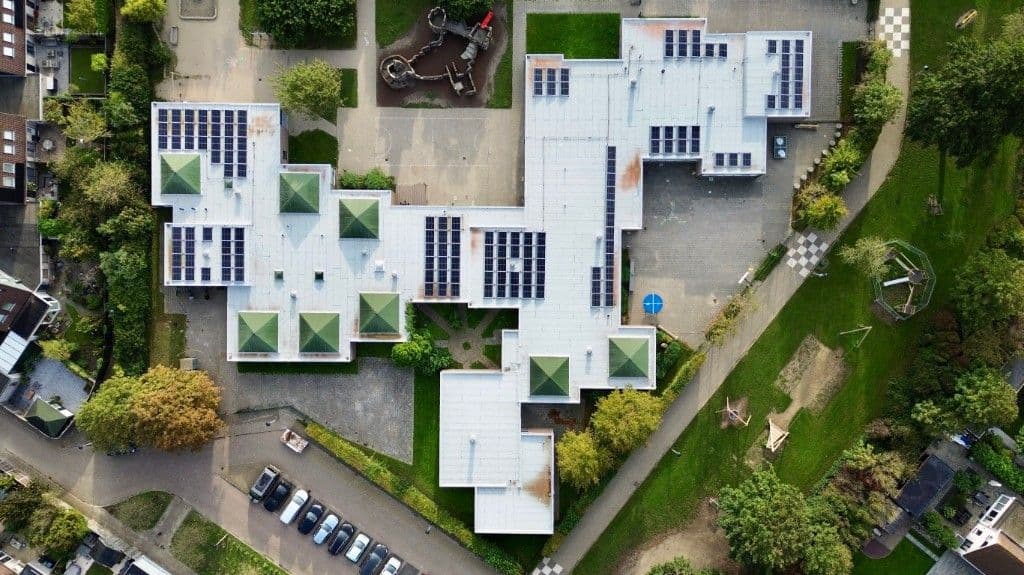 Luchtfoto van een schoolgebouw met zonnepanelen en groendaken